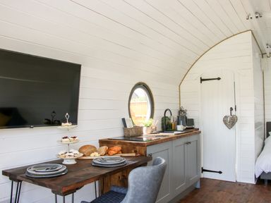 A kitchen area with a wooden table set with plates and food in a small white room at Withy Willows in Diddlebury near Ludlow
