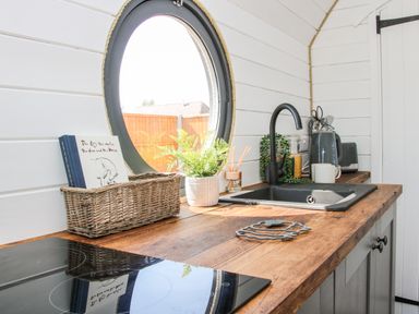 A kitchen countertop with a black sink and faucet a woven basket with books a potted plant various kitchen utensils and a round window at Withy Willows in Diddlebury near Ludlow