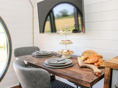 A dining table with plates and cutlery a three tier cake stand with pastries and a wooden board with bread and croissants in a room with a wall mounted television at Withy Willows in Diddlebury near Ludlow