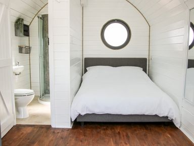 A bedroom with a double bed and a circular window next to a bathroom with a toilet and shower at Withy Willows Diddlebury near Ludlow