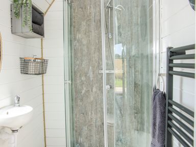 A bathroom with a glass shower enclosure a small white sink a wall shelf with towels and a towel rack with a hanging towel at Withy Willows in Diddlebury near Ludlow