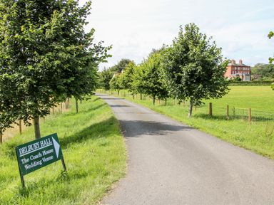 A paved driveway with trees on both sides leading to a large brick building with a sign for Delbury Hall wedding venue at Diddlebury near Ludlow