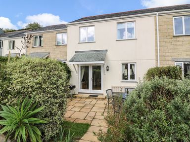 A garden patio with table and chairs and a barbecue outside a two story house at Oyster Cottage in Falmouth
