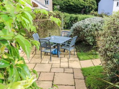 An outdoor patio with a metal table and four chairs surrounded by green bushes at Oyster Cottage in Falmouth
