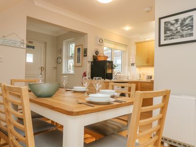 A dining table set with bowls glasses and cutlery in a kitchen with wooden chairs and cabinets at Oyster Cottage in Falmouth