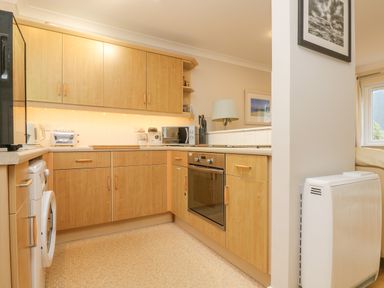 A kitchen with wooden cabinets an oven microwave and washing machine at Oyster Cottage in Falmouth