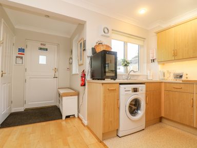 A kitchen with wooden cabinets washing machine toaster and kettle near a white door at Oyster Cottage in Falmouth