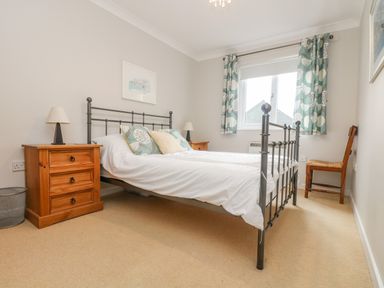 A bedroom with a metal frame bed with white bedding two wooden bedside tables with lamps patterned curtains and a wooden chair by the window at Oyster Cottage in Falmouth