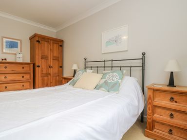 A bedroom with a bed and pillows a wooden wardrobe chest of drawers and bedside tables with lamps at Oyster Cottage in Falmouth