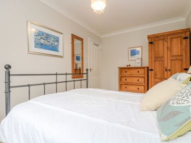 A bedroom with a metal bed frame white bedding wooden wardrobe and chest of drawers at Oyster Cottage in Falmouth