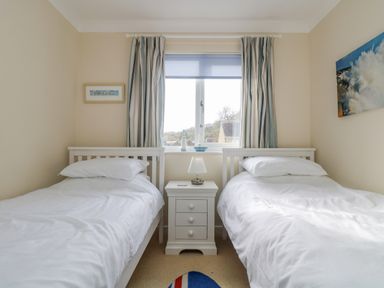A bedroom with two single beds separated by a white nightstand under a window with curtains at Oyster Cottage in Falmouth