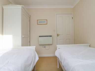 A bedroom with two single beds a white wardrobe a heater on the wall and a framed picture above the heater at Oyster Cottage in Falmouth