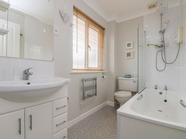 A bathroom with a sink, mirror, bathtub with shower, toilet, and window with blinds at Oyster Cottage in Falmouth