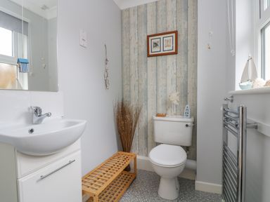 A bathroom with a white sink and cabinet a wooden bench a toilet with decorations and a radiator at Oyster Cottage in Falmouth