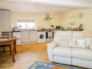 An open plan kitchen and living room with a white sofa and wooden dining table at Woodpecker Lodge in Henley near Langport