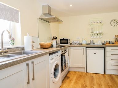A kitchen with a washing machine sink microwave kettle and cutting boards at Woodpecker Lodge in Henley near Langport