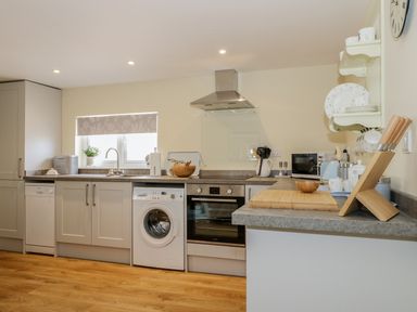 A kitchen with washing machine oven countertop and shelves at Woodpecker Lodge in Henley near Langport