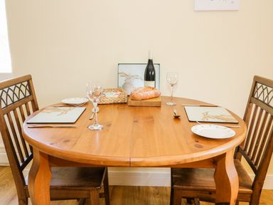 A wooden dining table with two wooden chairs set with plates wine glasses bread and a wine bottle at Woodpecker Lodge in Henley near Langport