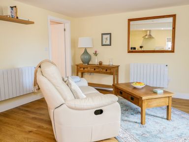 A living room with a cream sofa wooden coffee table with a fruit bowl a console table with a lamp and a mirror on the wall at Woodpecker Lodge in Henley near Langport