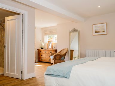 A bedroom with a bed a wicker chair a wooden dresser with a mirror and a tall decorative mirror at Woodpecker Lodge Henley near Langport
