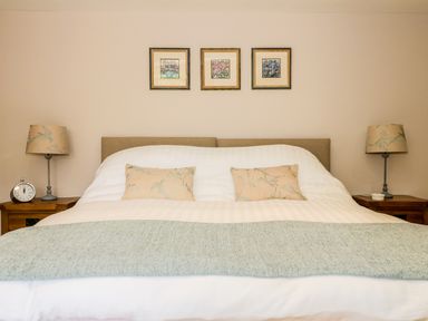 A bedroom with a bed with cushions and a blue throw blanket with bedside tables and lamps at Woodpecker Lodge Henley near Langport