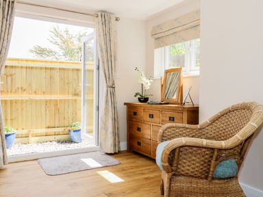 A room with wicker chair wooden dresser mirror and open door leading outside at Woodpecker Lodge in Henley near Langport