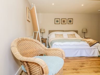 A bedroom with a wicker chair a double bed bedside tables and framed pictures on the wall at Woodpecker Lodge in Henley near Langport