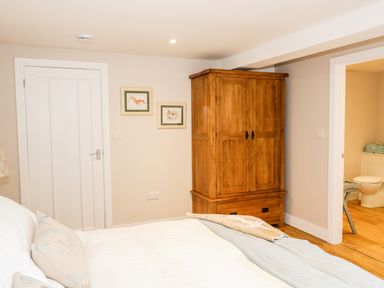 A bedroom with a wooden wardrobe white door and partially visible bathroom at Woodpecker Lodge in Henley near Langport