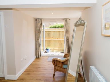 A room with an open door leading outside a wooden chair a tall mirror and curtains at Woodpecker Lodge in Henley near Langport