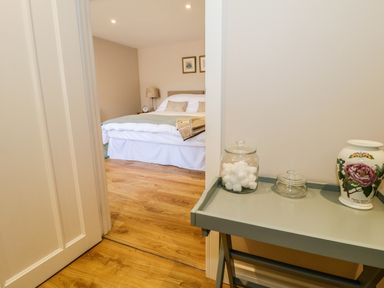 A bedroom with a bed and bedside table seen through an open door and a tray table with jars and a vase nearby at Woodpecker Lodge in Henley near Langport