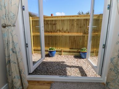 A view through open glass doors to a small gravel area with two blue flower pots and a wooden fence at Woodpecker Lodge in Henley near Langport