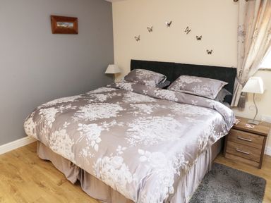 A bedroom with a bed with floral bedding a bedside table with a lamp and butterfly wall decals at Knott Lodge in Sedbergh