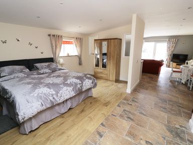 A bedroom with a bed a wardrobe and curtains leading to a living area at Knott Lodge in Sedbergh