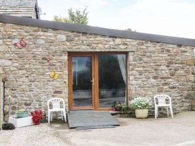 Stone wall with a wooden framed glass door two white plastic chairs and several potted plants Knott Lodge Sedbergh