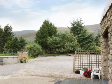 An outdoor area with gravel ground potted plants white chair lattice fence stone wall and trees in the background at Knott Lodge Sedbergh