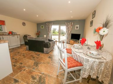 A living room with a dining table set with red napkins and floral dishes a sofa a television and kitchen cabinets at Knott Lodge in Sedbergh