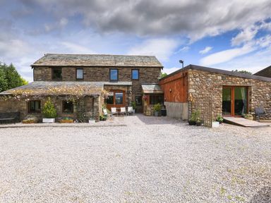A stone house with a gravel courtyard and outdoor chairs at Knott Lodge in Sedbergh
