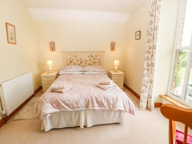 A bedroom with a double bed two bedside tables with lamps floral curtains and framed pictures at Dinas Farmhouse Annex in Caernarfon