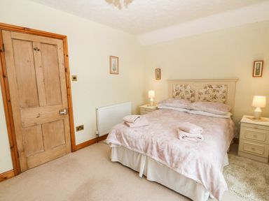 A bedroom with a double bed with floral headboard two bedside tables with lamps and folded towels on the bed at Dinas Farmhouse Annex in Caernarfon
