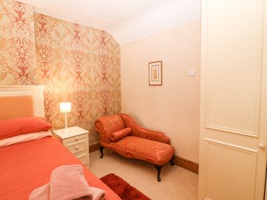A bedroom with an orange bedspread a white bedside table with a lamp patterned wallpaper and an orange chaise lounge at Dinas Farmhouse Annex in Caernarfon