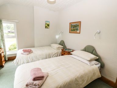 A bedroom with two single beds and a small wooden nightstand between them at Dinas Farmhouse Annex in Caernarfon