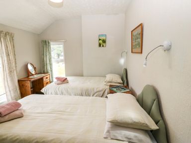A bedroom with two single beds, a wooden dressing table with a mirror, curtains on windows and framed pictures on the walls at Dinas Farmhouse Annex in Caernarfon