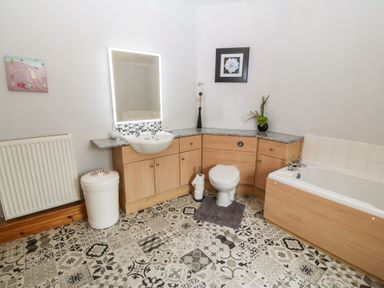 A bathroom with a sink, toilet, bathtub, and a patterned floor at Dinas Farmhouse Annex in Caernarfon
