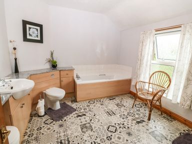 A bathroom with a bathtub sink toilet patterned floor and a wicker chair at Dinas Farmhouse Annex in Caernarfon