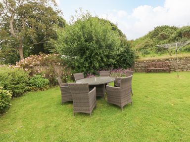 A garden with a round table and six chairs on grass near bushes and flowers at Dinas Farmhouse Annex in Caernarfon