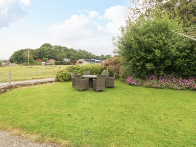 A garden area with a round table and six chairs on grass surrounded by bushes and flowers at Dinas Farmhouse Annex in Caernarfon