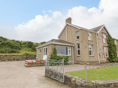 Exterior view of a two-story house with a stone and stucco facade a metal gate and driveway at Dinas Farmhouse Annex in Caernarfon