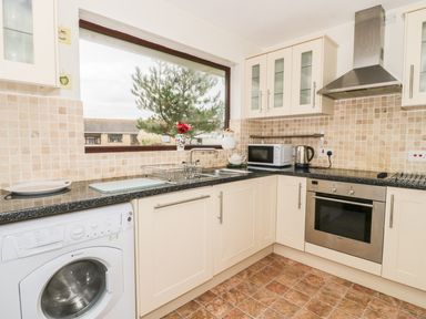 A kitchen with cream cabinets a washing machine a microwave an oven a kettle a sink and tiled walls at Dehangfa in Fairbourne