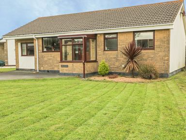 A front view of a single-story house with a lawn and small garden at Dehangfa in Fairbourne