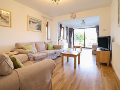 A living room with beige sofas wooden tables a television and sliding glass doors at Dehangfa in Fairbourne
